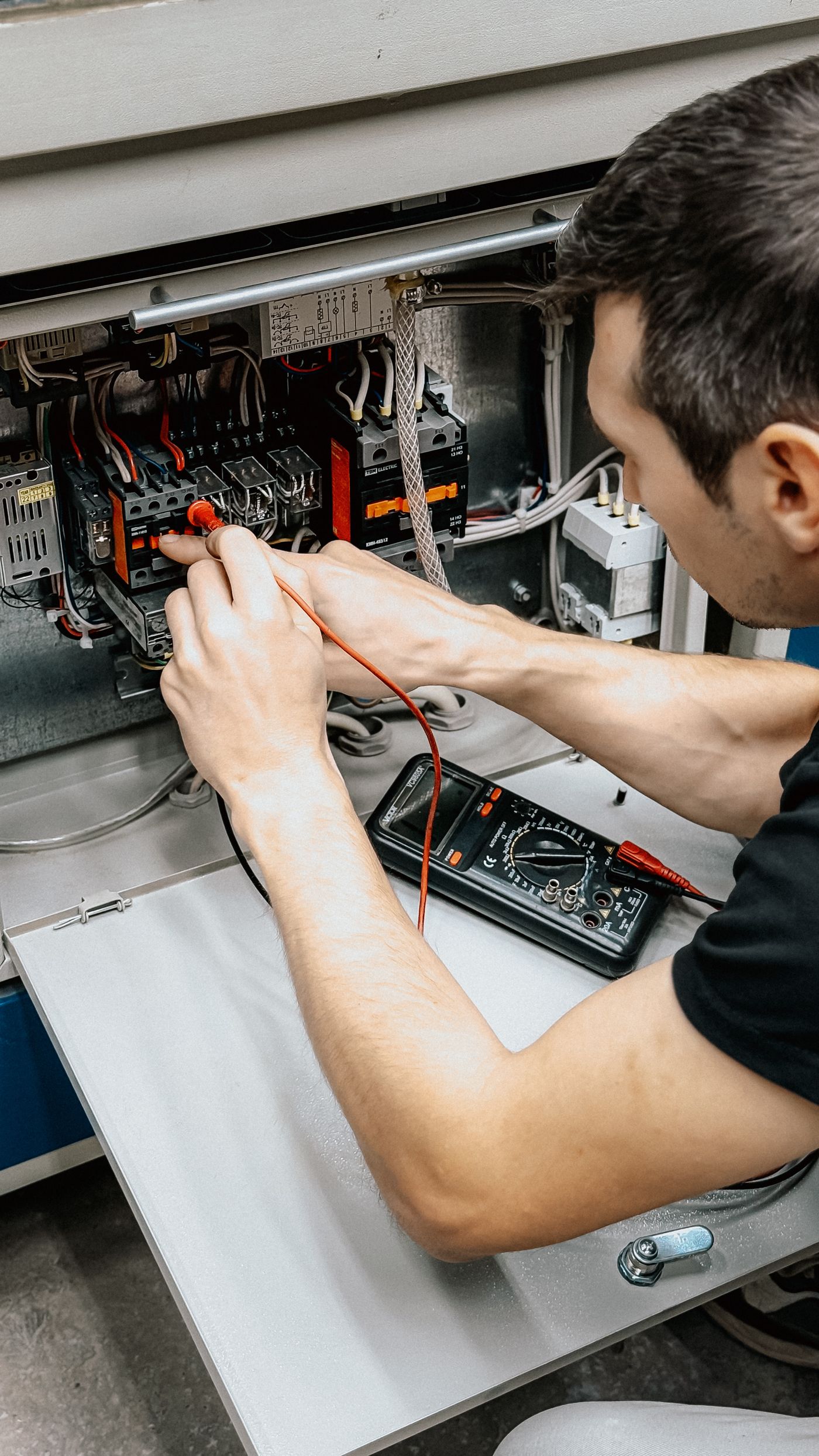 Electrician testing connections in an open panel with a multimeter