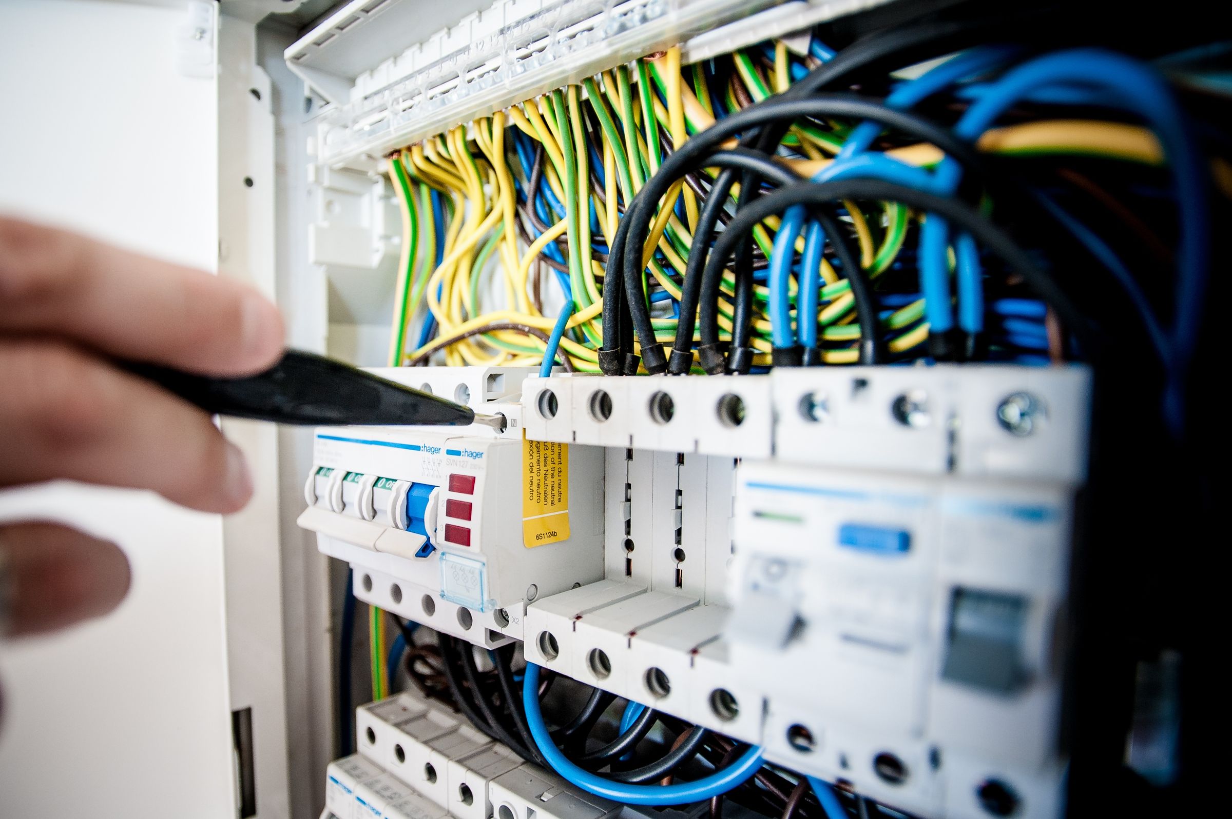 Close-up of an electrician's hands working on wiring inside an open distribution board