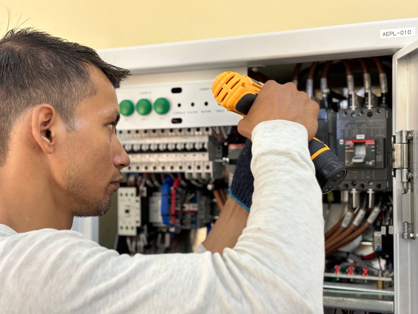 Electrician drilling a fixing next to an open circuit breaker panel